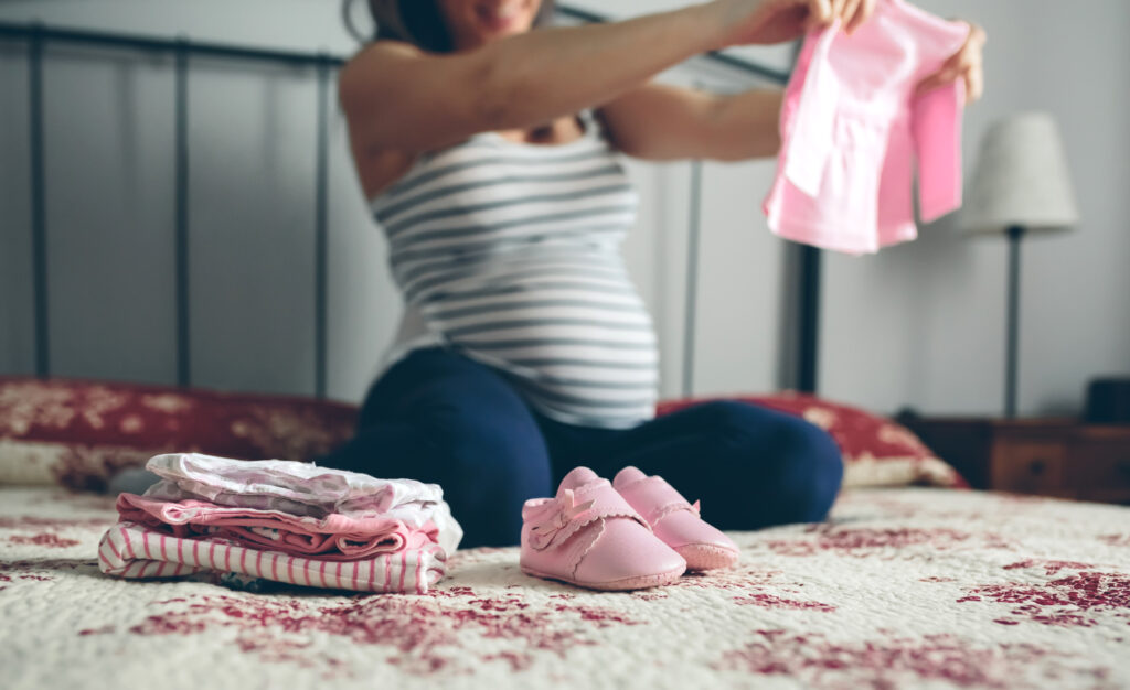Schwangere Frau sortiert Babykleidung