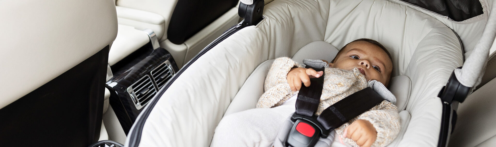 Mutter auf dem Fahrersitz ihres Autos, die über die Schulter auf ihr Baby in der Calmi R129 blickt