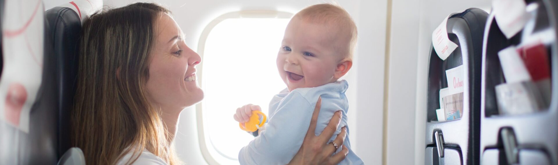 Mutter hält ihr Baby im Flugzeug auf dem Schoß – Fliegen mit Baby stressfrei gestalten.