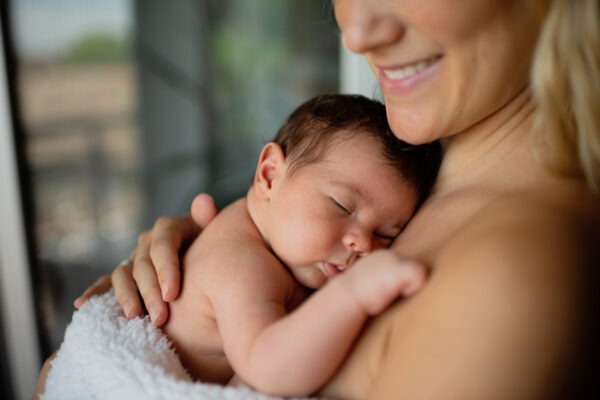 Eine glückliche Mama hält ihr Neugeborenes nach der Geburt im Krankenhaus oder Geburtshaus liebevoll in den Armen.