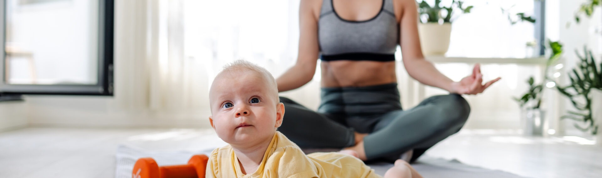Junge Mutter meditiert in Sportkleidung mit Baby vor sich.