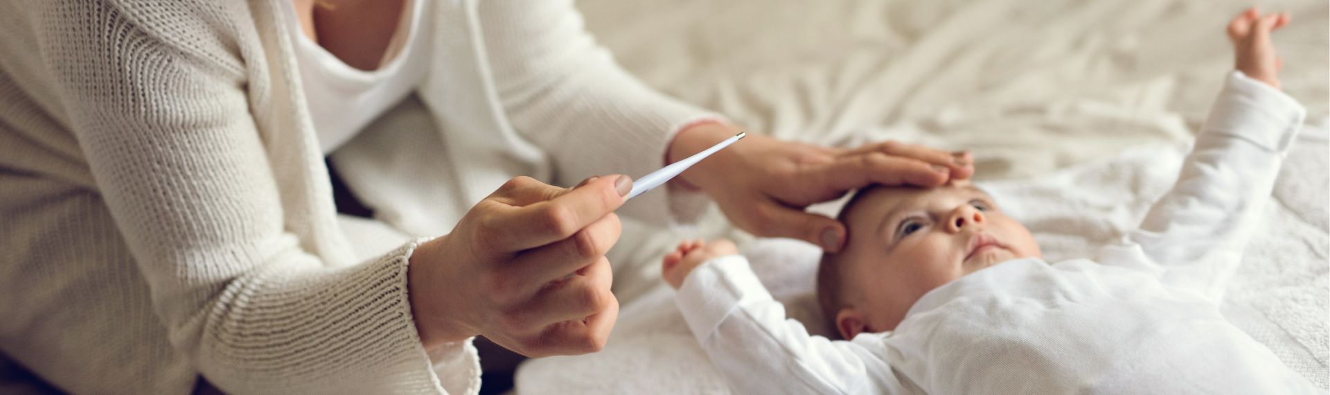 Frau misst die Temperatur eines Babys mit einem Thermometer, während sie die Hand auf dessen Stirn legt.