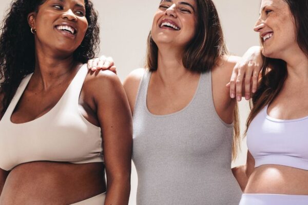 Drei werdende Mamas, die Zeit miteinander verbringen und lachen. Man sieht ihnen ihre körperlichen Veränderungen in der Schwangerschaft an.