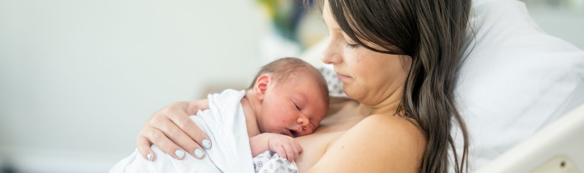 Eine Frau liegt in einem Krankenhausbett und hält ihr neugeborenes Baby liebevoll in den Armen, während das Baby auf ihrer Brust schläft.