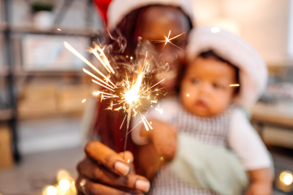 Eine Mutter schaut mit ihrem Baby eine Wunderkerze an. Mutter und Baby sind in der Unschärfe zu sehen.