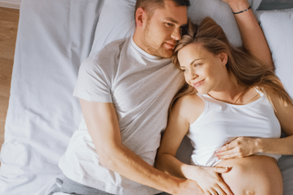 Schwangeres Paar liegt entspannt im Bett und halten den Bauch der Frau.