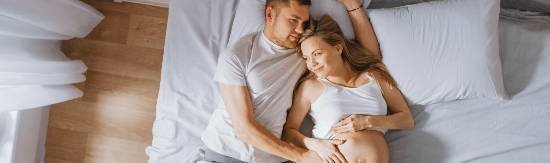 Schwangeres Paar liegt entspannt im Bett und halten den Bauch der Frau.