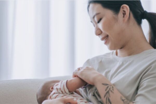 Eine Mutter stillt ihr Kind in einem leicht abgedunkelten Raum, die beiden haben eine innige und positive Stillbeziehung.