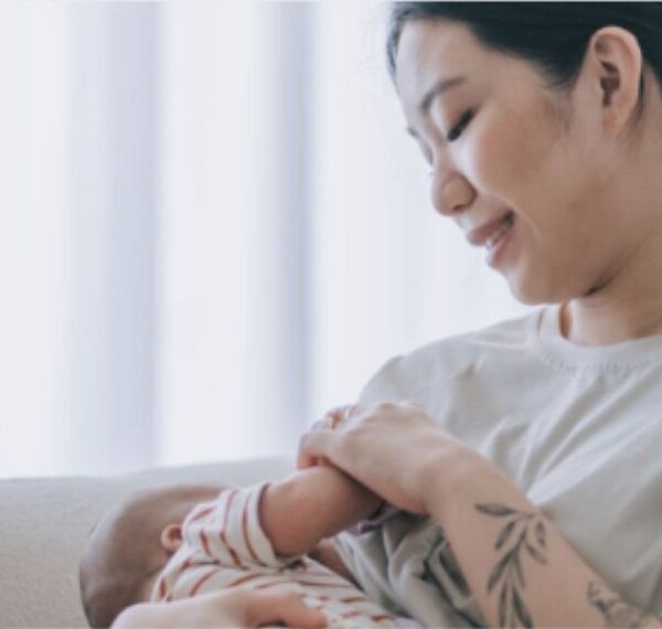 Eine Mutter stillt ihr Kind in einem leicht abgedunkelten Raum, die beiden haben eine innige und positive Stillbeziehung.