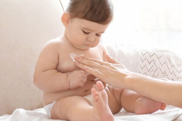 Mutter cremt ihr Baby sanft ein.