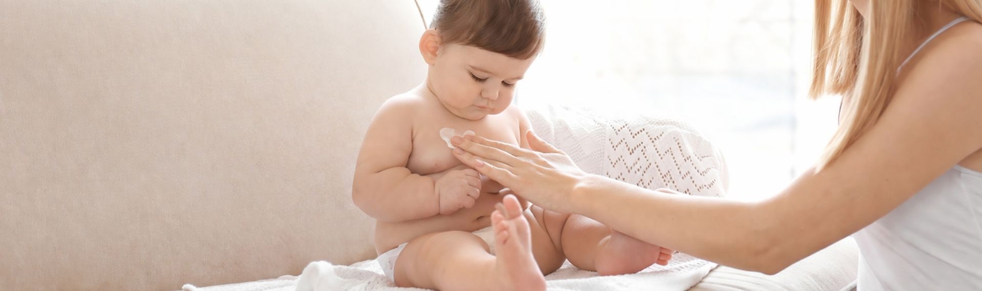 Mutter cremt ihr Baby sanft ein.