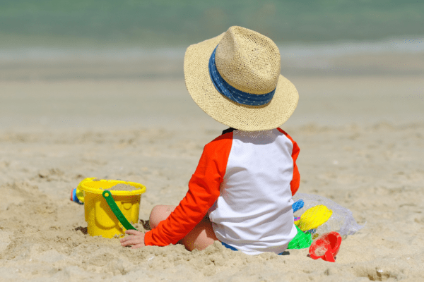 Kind mit Sonnenhut und Spielzeug am Strand
