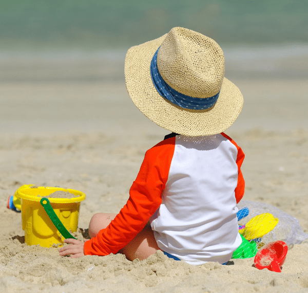 Kind mit Sonnenhut und Spielzeug am Strand