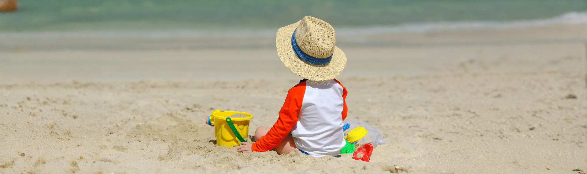 Kind mit Sonnenhut und Spielzeug am Strand